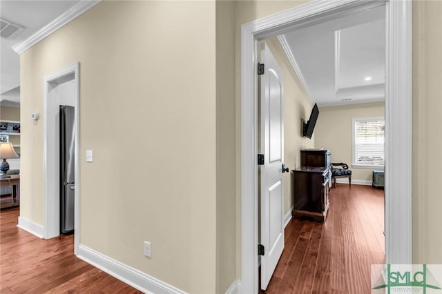 hall featuring ornamental molding, a raised ceiling, and wood-type flooring