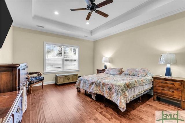 bedroom with ceiling fan, ornamental molding, wood-type flooring, and a raised ceiling