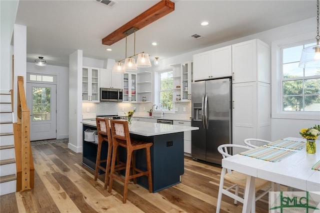 kitchen featuring hanging light fixtures, a kitchen island, white cabinets, and appliances with stainless steel finishes