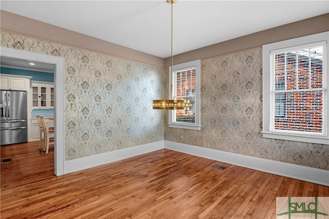 unfurnished room with baseboards, visible vents, wallpapered walls, and light wood-style floors