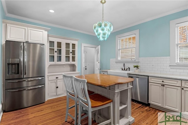 kitchen with ornamental molding, a sink, white cabinets, appliances with stainless steel finishes, and light wood-type flooring