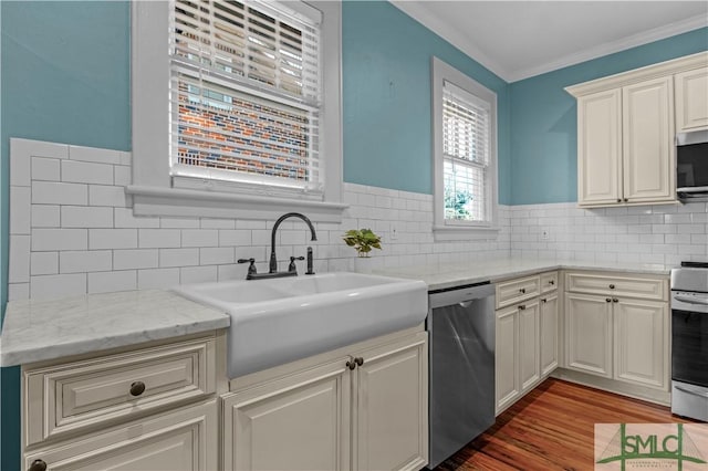 kitchen featuring ornamental molding, light stone counters, appliances with stainless steel finishes, wood finished floors, and a sink