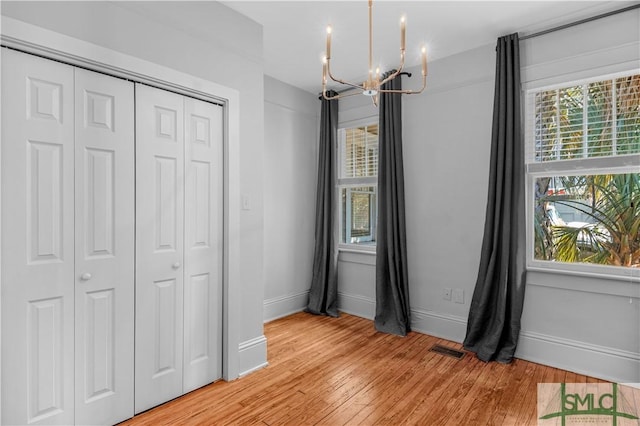 unfurnished bedroom featuring a notable chandelier, visible vents, multiple windows, and light wood-style floors