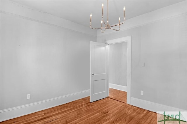 spare room featuring an inviting chandelier, wood finished floors, and baseboards