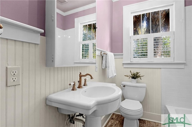 bathroom featuring crown molding, a wainscoted wall, toilet, a bathtub, and a sink