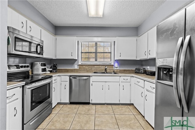 kitchen with appliances with stainless steel finishes, sink, white cabinets, light tile patterned floors, and a textured ceiling