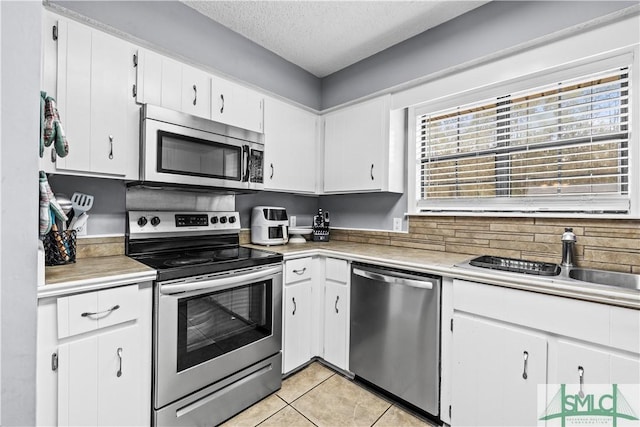 kitchen featuring sink, white cabinetry, stainless steel appliances, a textured ceiling, and light tile patterned flooring