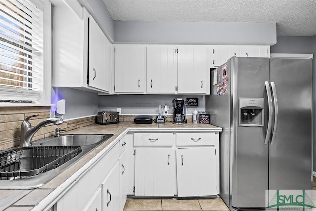 kitchen featuring sink, light tile patterned floors, stainless steel fridge, white cabinetry, and a textured ceiling