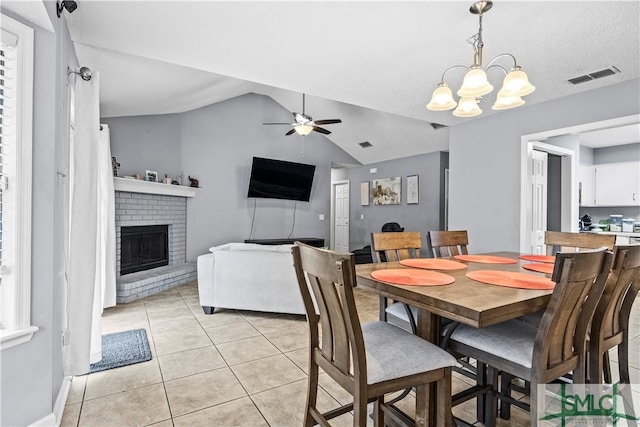 dining area with light tile patterned flooring, a brick fireplace, ceiling fan with notable chandelier, and lofted ceiling