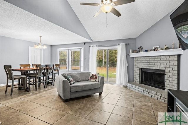 tiled living room with ceiling fan with notable chandelier, vaulted ceiling, a brick fireplace, and a textured ceiling