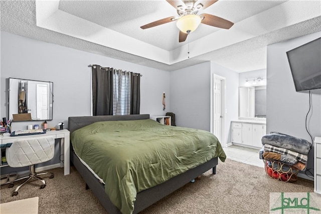 carpeted bedroom featuring a raised ceiling, ceiling fan, a textured ceiling, and ensuite bath