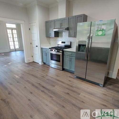 kitchen with ornamental molding, appliances with stainless steel finishes, light wood-type flooring, and backsplash