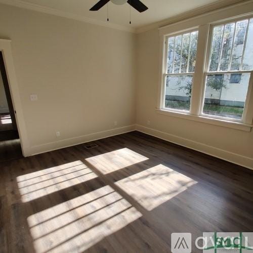 empty room with ornamental molding, dark wood-type flooring, and ceiling fan