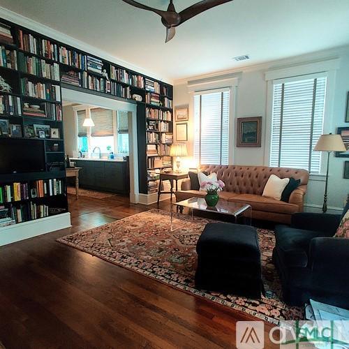 living room with wood-type flooring, ornamental molding, and ceiling fan