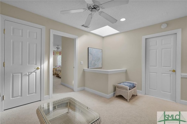 interior space featuring light carpet, ceiling fan, a skylight, and a textured ceiling