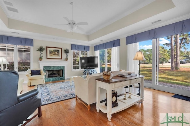 living room featuring ceiling fan, wood-type flooring, a raised ceiling, and a high end fireplace