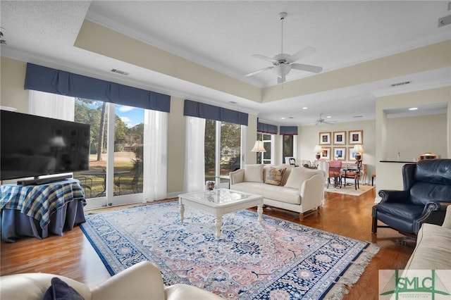 living room with a raised ceiling, ornamental molding, wood-type flooring, and ceiling fan