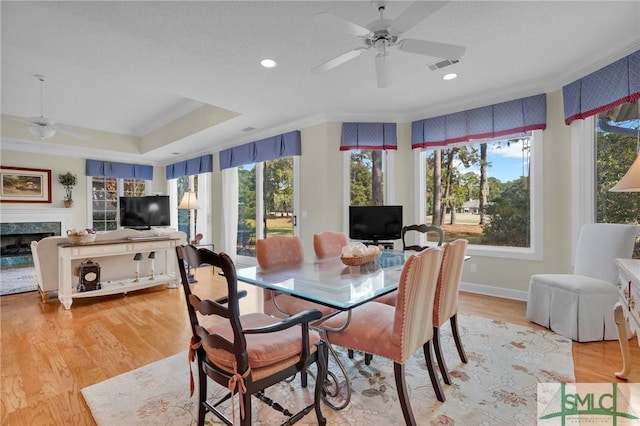 dining area with a fireplace, light hardwood / wood-style flooring, a raised ceiling, and ceiling fan