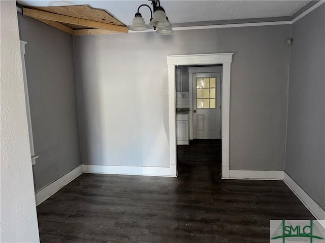 empty room with ornamental molding, dark hardwood / wood-style floors, a textured ceiling, and a chandelier