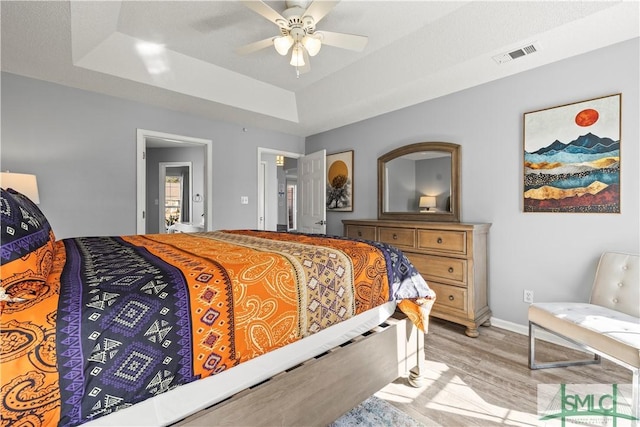 bedroom with a tray ceiling, light hardwood / wood-style flooring, and ceiling fan