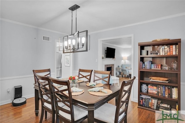 dining room featuring crown molding, a brick fireplace, an inviting chandelier, and light wood-type flooring