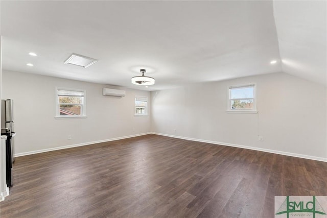 empty room featuring a wall mounted air conditioner, vaulted ceiling, dark hardwood / wood-style floors, and a healthy amount of sunlight