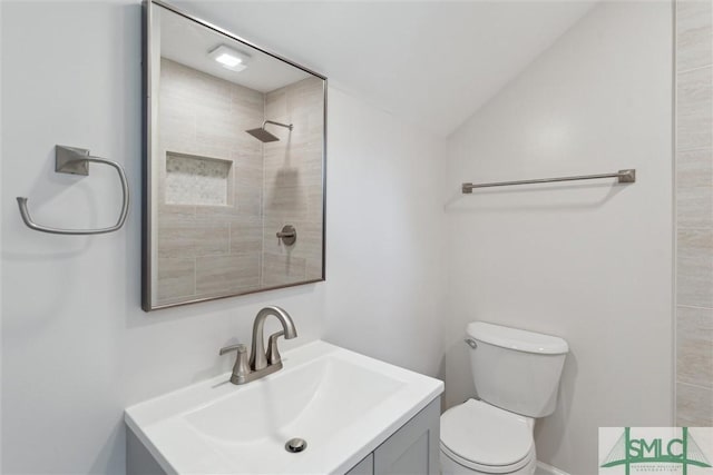 bathroom with vanity, lofted ceiling, tiled shower, and toilet