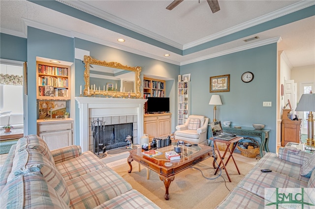 carpeted living room featuring a tiled fireplace, crown molding, and built in features