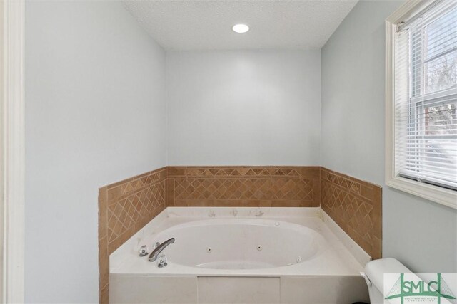 bathroom featuring toilet, tiled bath, and a textured ceiling