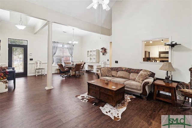 living room with ornate columns, a high ceiling, dark wood-type flooring, and ceiling fan with notable chandelier