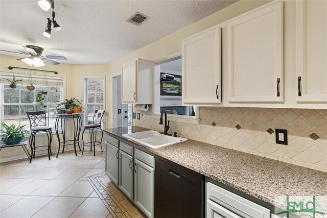 kitchen featuring tasteful backsplash, white cabinetry, black dishwasher, sink, and light tile patterned floors