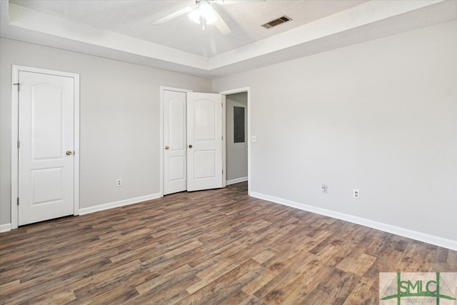 spare room with a tray ceiling, dark wood-type flooring, electric panel, and ceiling fan