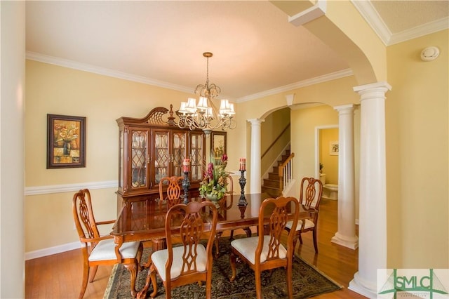 dining area with hardwood / wood-style flooring, crown molding, decorative columns, and a notable chandelier