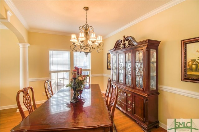 dining area featuring crown molding, a notable chandelier, light hardwood / wood-style floors, and ornate columns