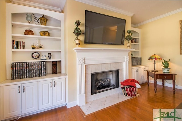 sitting room featuring ornamental molding, a tiled fireplace, built in features, and light wood-type flooring