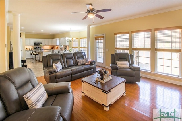 living room with crown molding, ceiling fan with notable chandelier, light hardwood / wood-style floors, and ornate columns