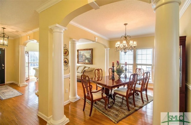 dining area with hardwood / wood-style flooring, crown molding, a chandelier, and ornate columns