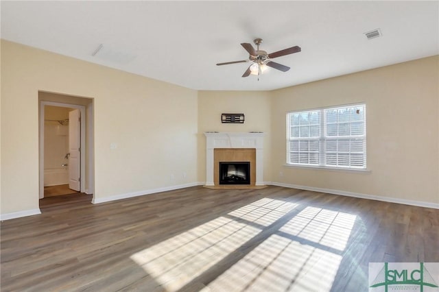 unfurnished living room featuring ceiling fan, wood-type flooring, and a tiled fireplace