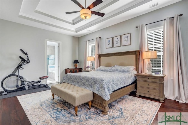 bedroom featuring dark hardwood / wood-style flooring, a tray ceiling, ceiling fan, and ensuite bathroom