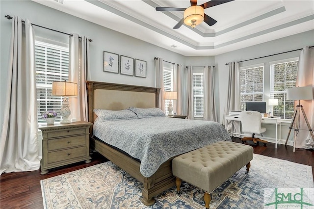 bedroom with ornamental molding, dark wood-type flooring, ceiling fan, and a tray ceiling