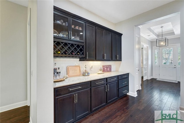 bar featuring dark wood-type flooring, backsplash, a tray ceiling, light stone countertops, and decorative light fixtures