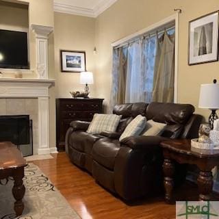 living room with hardwood / wood-style flooring, crown molding, a tiled fireplace, and ornate columns