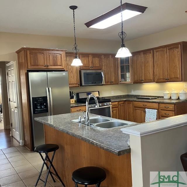 kitchen with a kitchen bar, sink, hanging light fixtures, light tile patterned floors, and appliances with stainless steel finishes