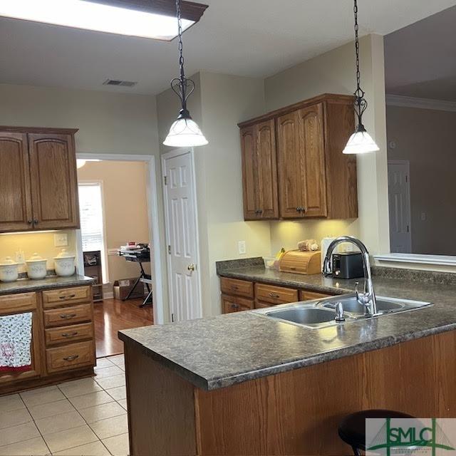 145 J Hendley Ct, Richmond Hill, GA 31324 - kitchen featuring brown cabinets, a sink, dark countertops, a peninsula, and hanging light fixtures
