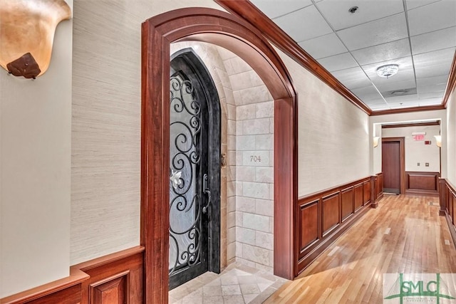 hallway with arched walkways, a drop ceiling, light wood-style floors, wainscoting, and crown molding