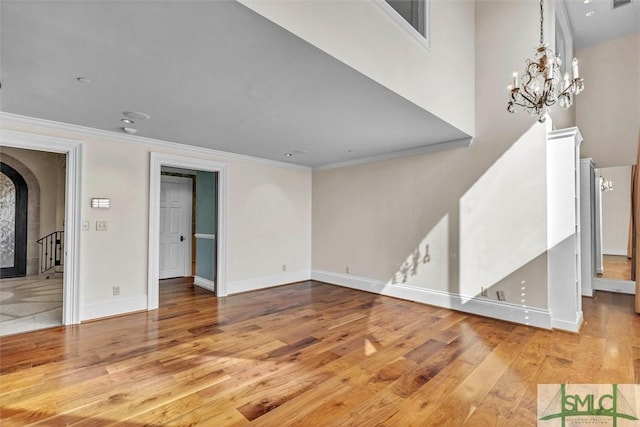 unfurnished living room featuring an inviting chandelier, crown molding, wood finished floors, and baseboards