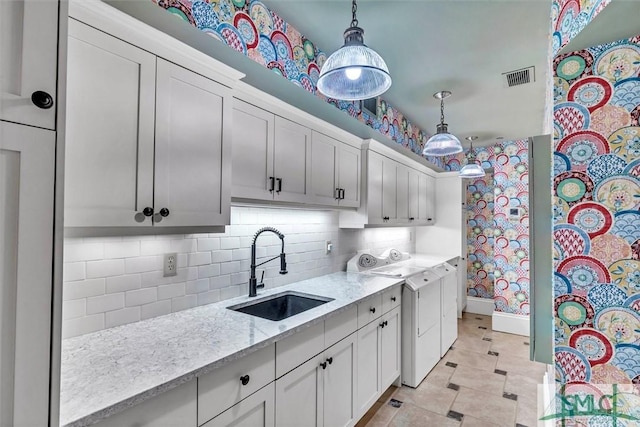 kitchen featuring visible vents, a sink, decorative light fixtures, decorative backsplash, and light stone countertops