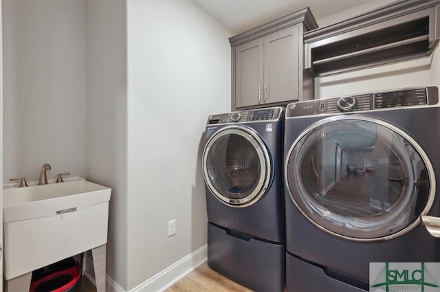 washroom featuring cabinets, separate washer and dryer, sink, and light hardwood / wood-style flooring