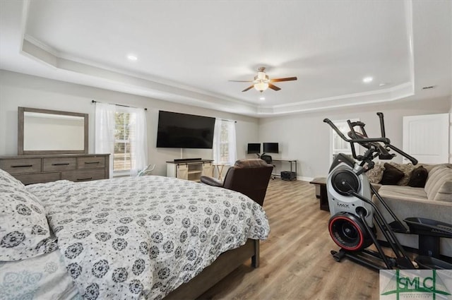 bedroom featuring ceiling fan, ornamental molding, a tray ceiling, and light hardwood / wood-style floors