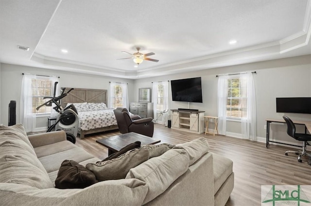 bedroom featuring multiple windows, light hardwood / wood-style flooring, and a raised ceiling